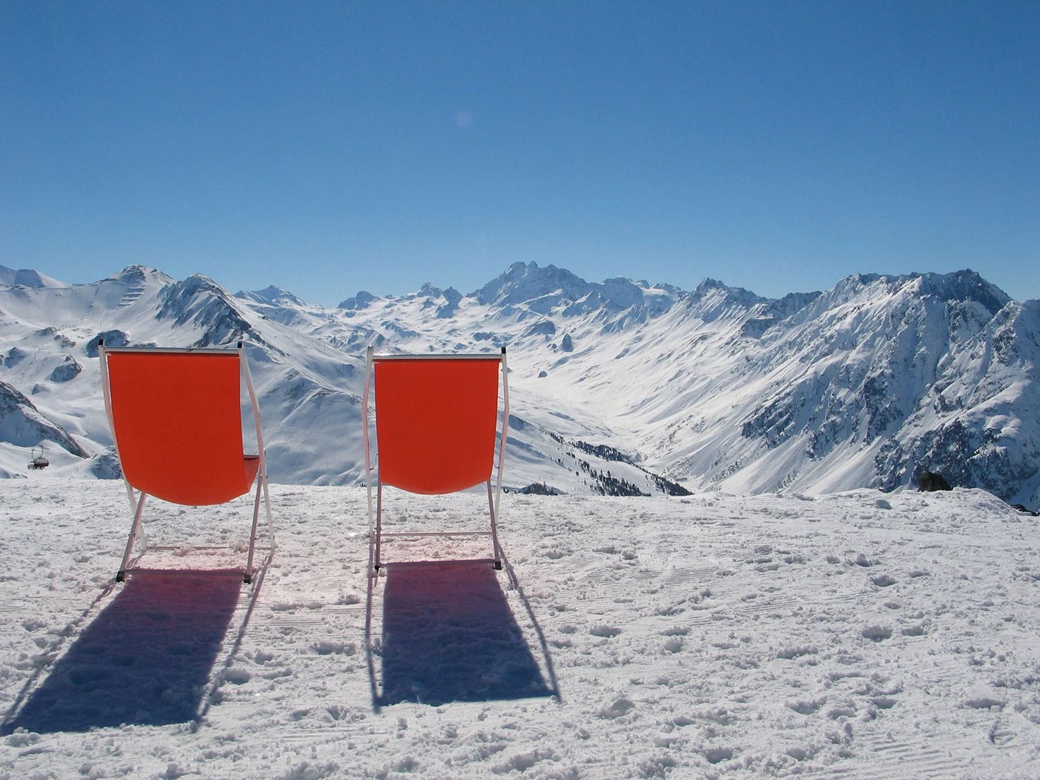 Orangene Liegestühle, zwei, auf Schnee vor verschneiten Bergen